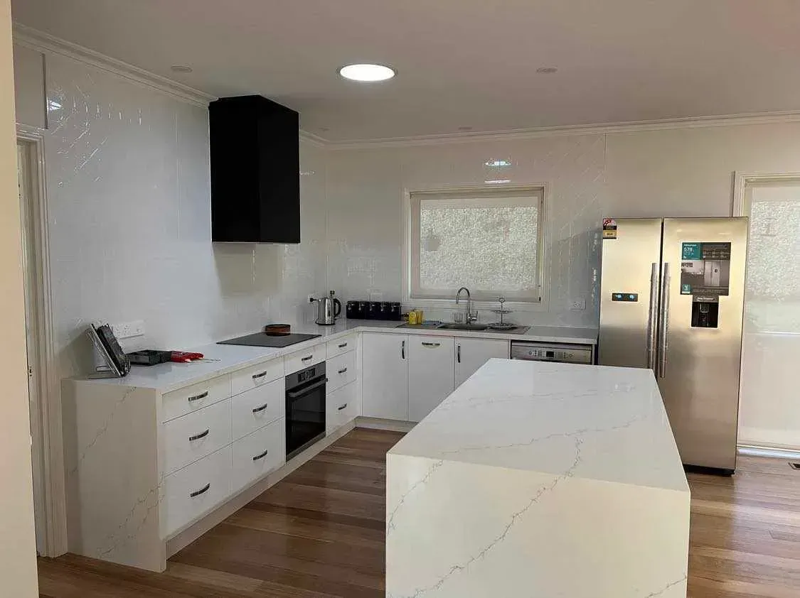 Bright white kitchen with island, cabinets, stainless fridge, and wood floors