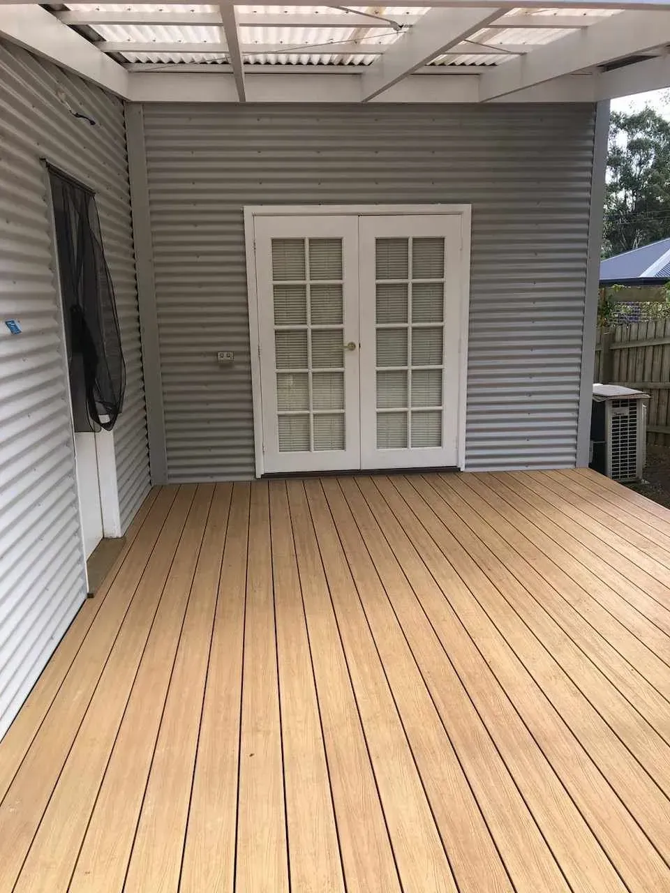 Covered wooden deck with gray siding, white French doors, and a black curtain on the left.