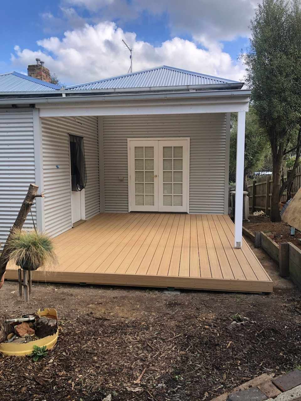 Back deck with new wooden flooring, white siding, and French doors under a blue metal roof