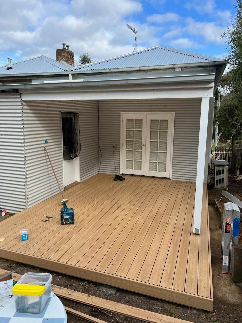 Wooden backyard deck under construction beside a white house with French doors and a patio roof