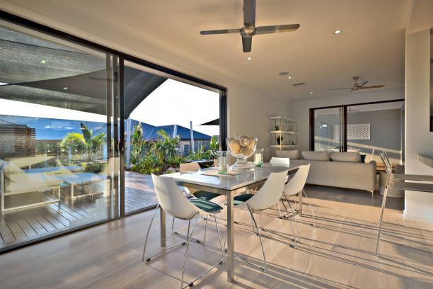Modern open-plan living and dining room with glass walls, white furniture, and a view of the pool and patio.