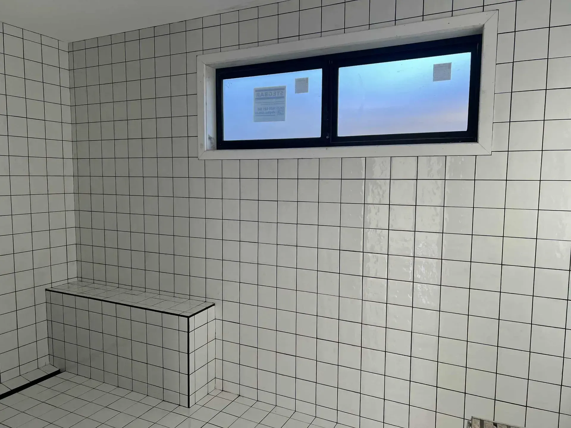 Small tiled room with a narrow horizontal window near the ceiling and a bench-like ledge on the left.