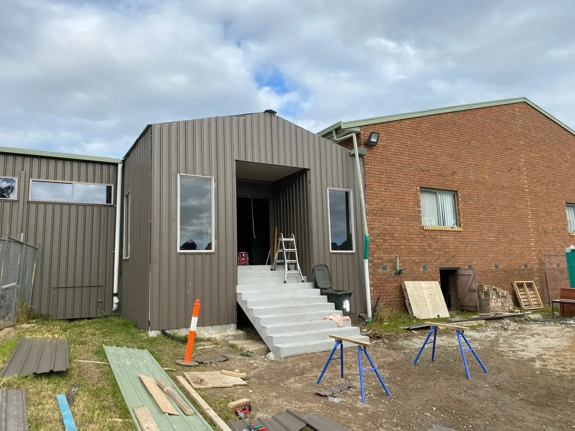 Partially built house exterior with dark siding, brick wall, and construction materials in front