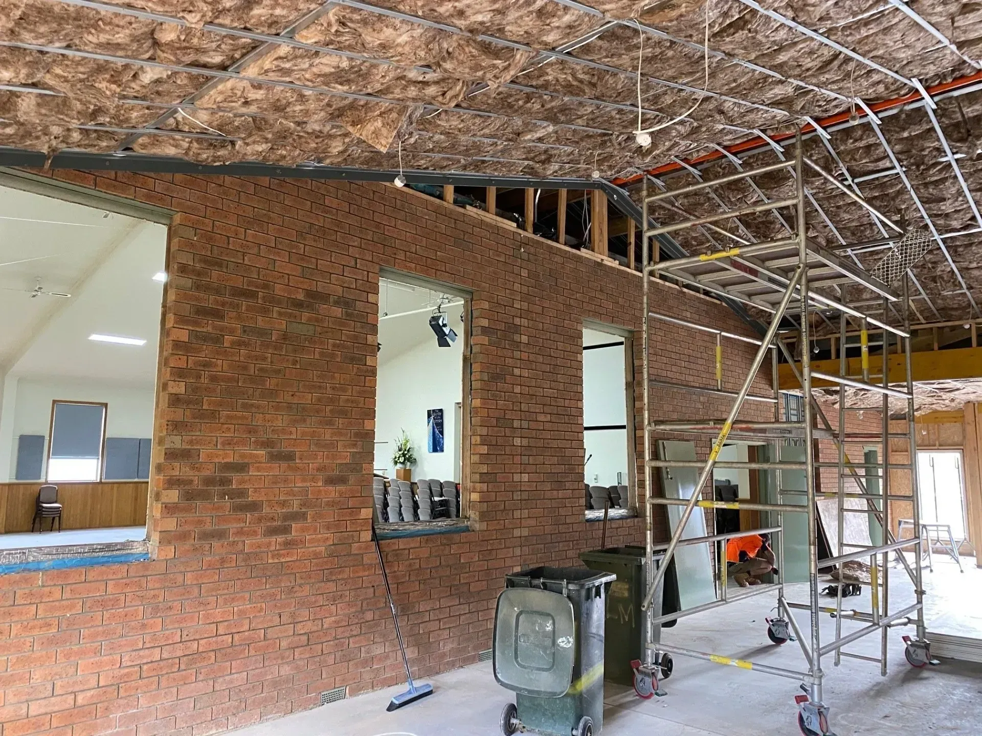 Interior of a brick building under construction with scaffolding, exposed ceiling, and tools on the floor