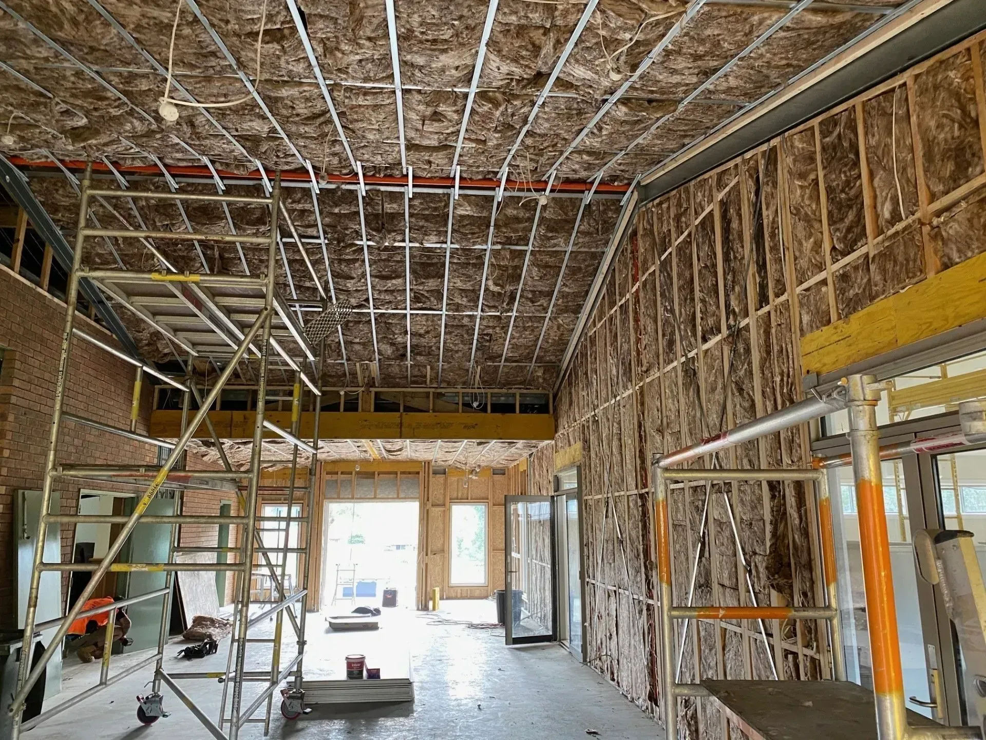 Renovation in progress inside a room with exposed insulation, scaffolding, and unfinished walls and ceiling.