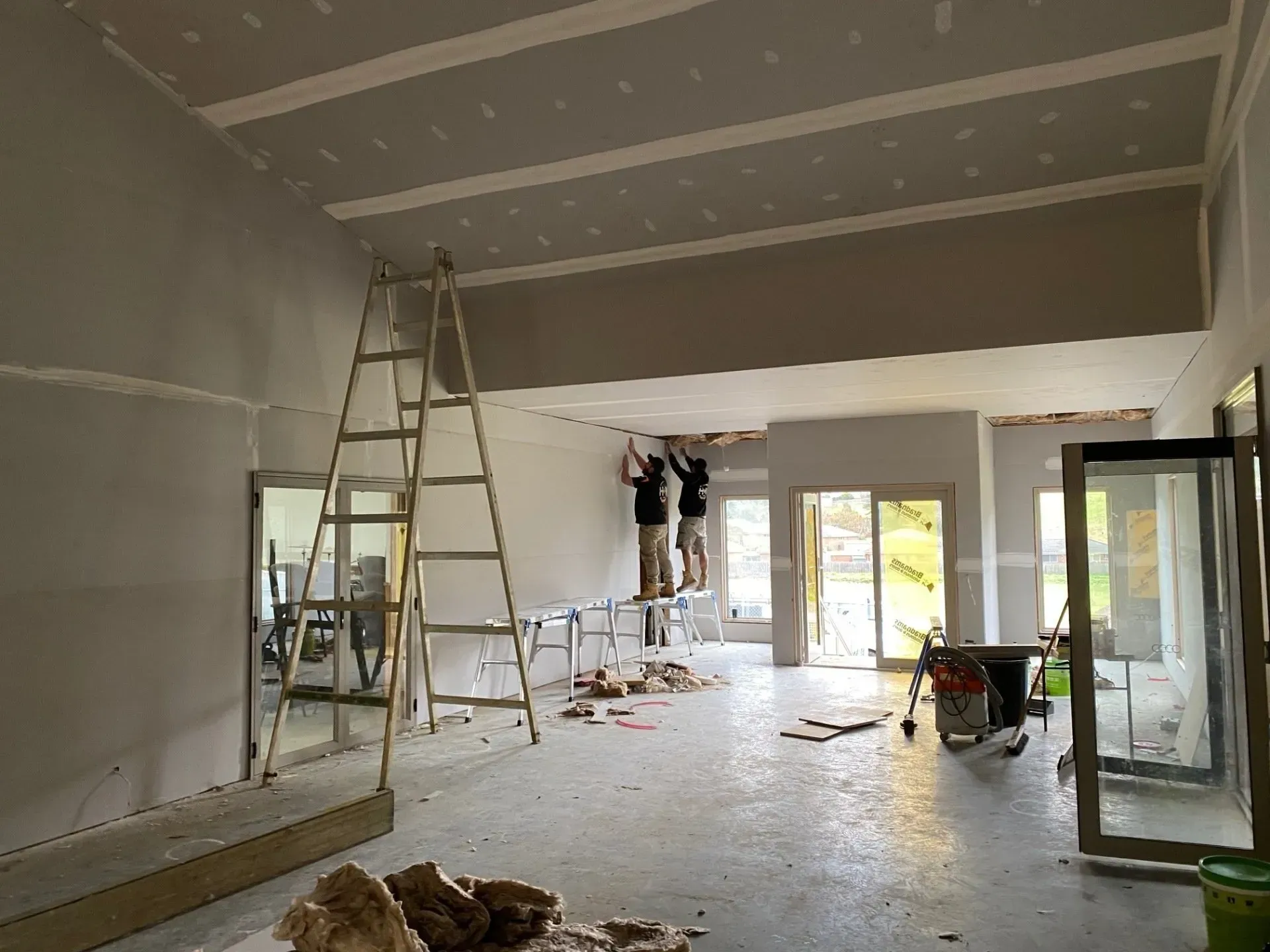 Partially renovated room with ladders, tools, and an open glass door during construction