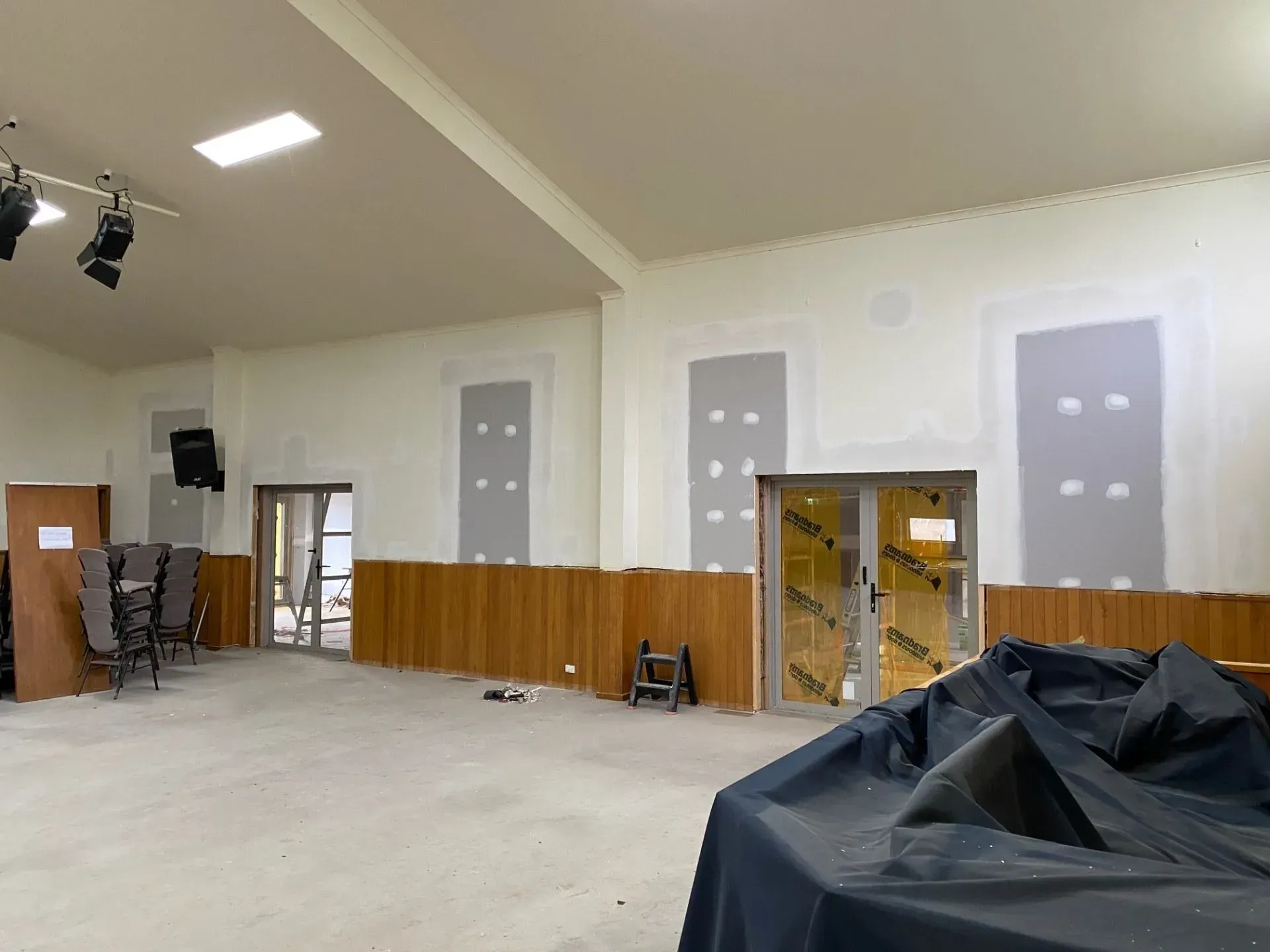 Large empty room with white walls, wood paneling, covered equipment, and exposed wall openings.