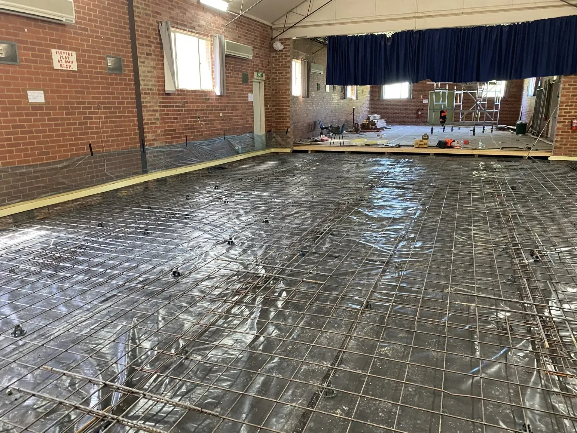 Large indoor hall with a wet concrete floor covered in a grid of wire mesh and brick walls.