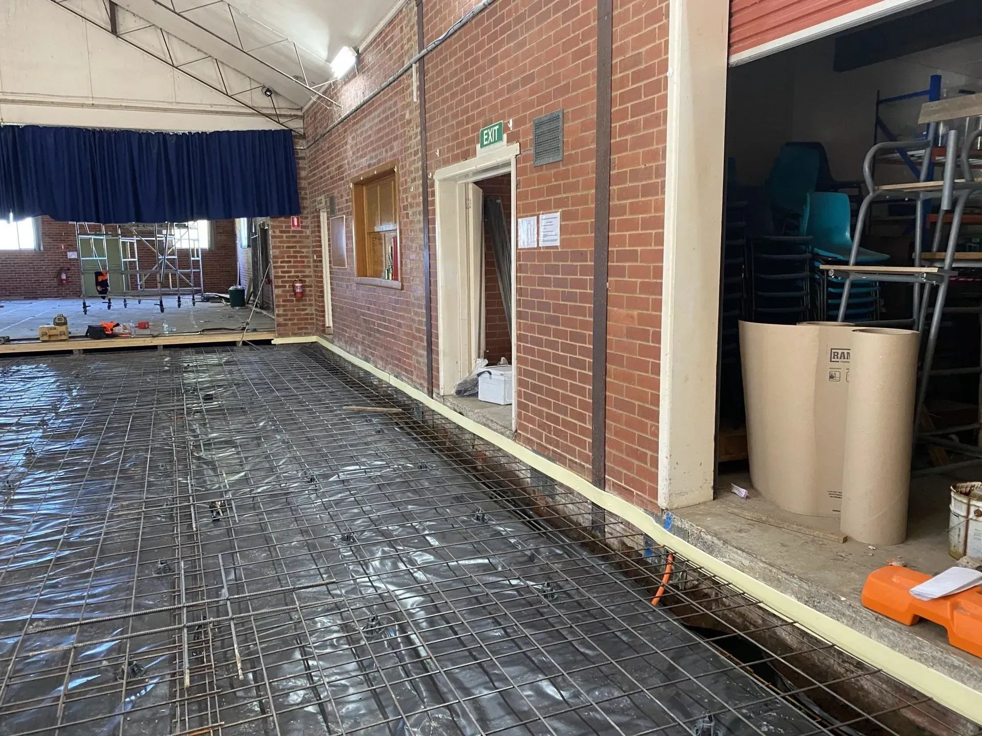 Indoor gym or hall with black floor covering, brick wall, open doorway, and stacked chairs and equipment.