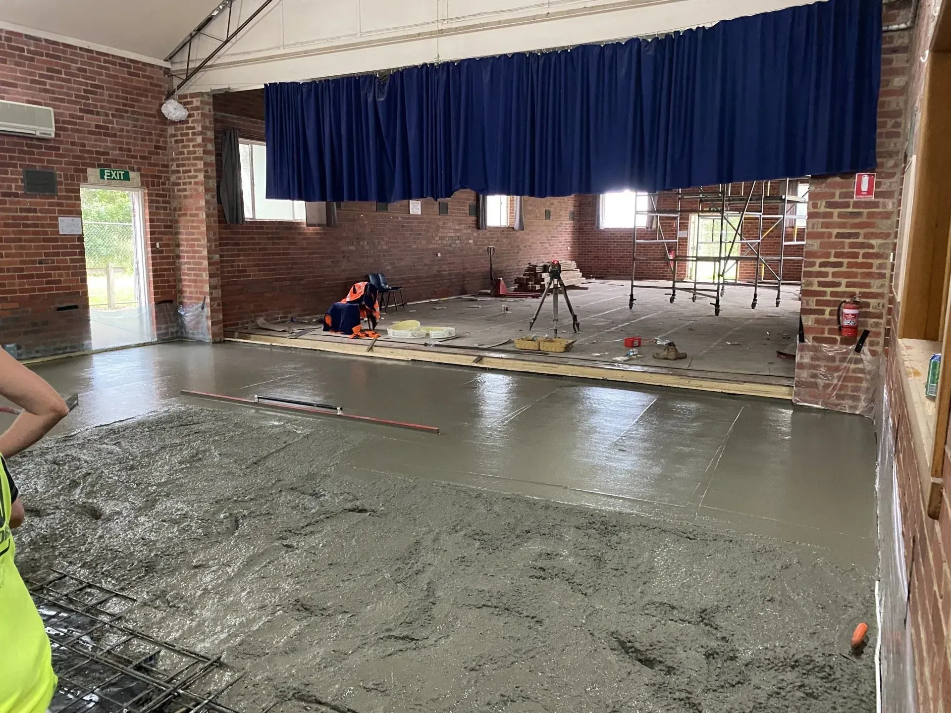 Workers smoothing wet concrete in a brick room with a blue stage curtain.