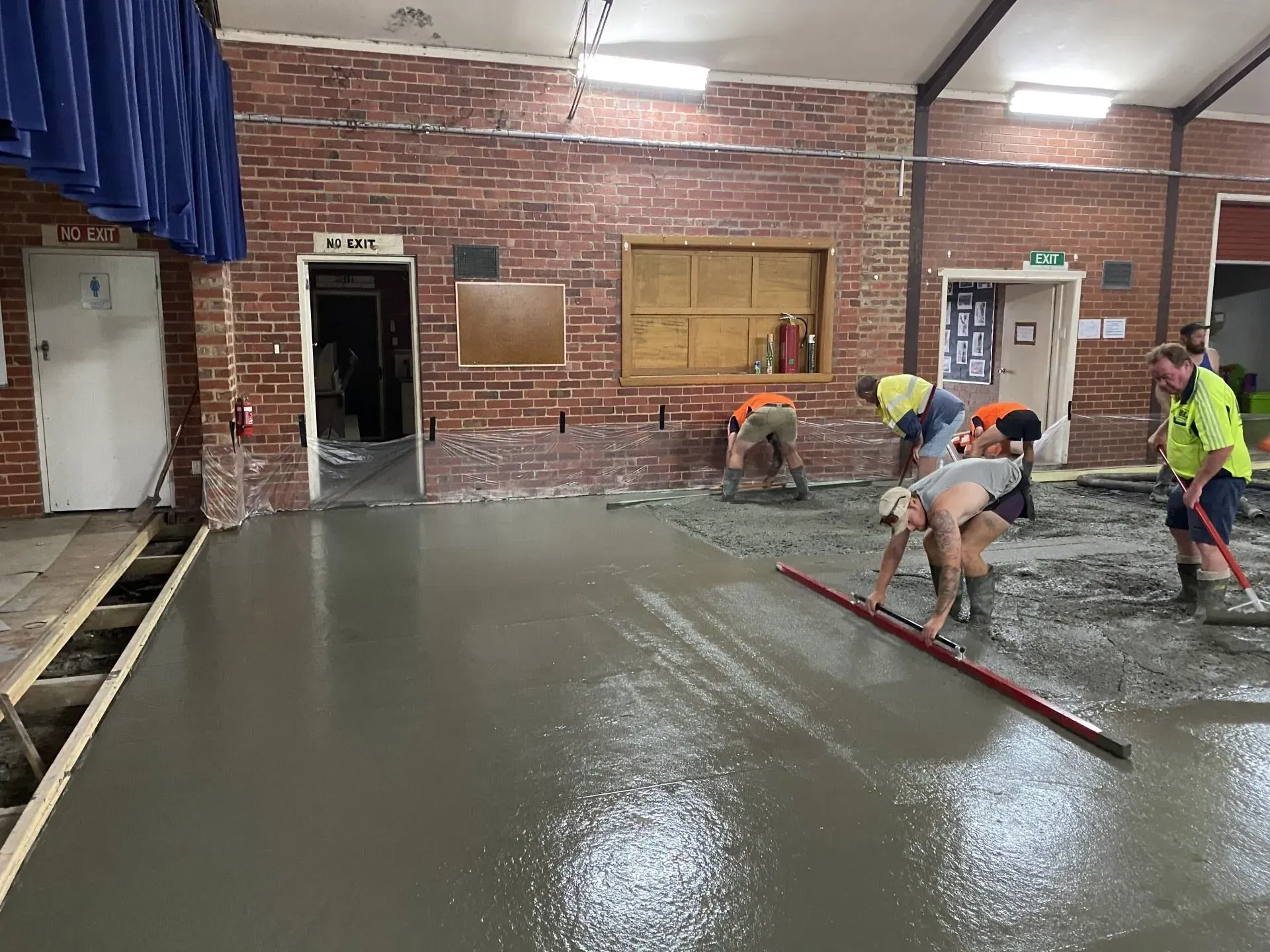 Workers leveling wet concrete in a brick-walled room under construction