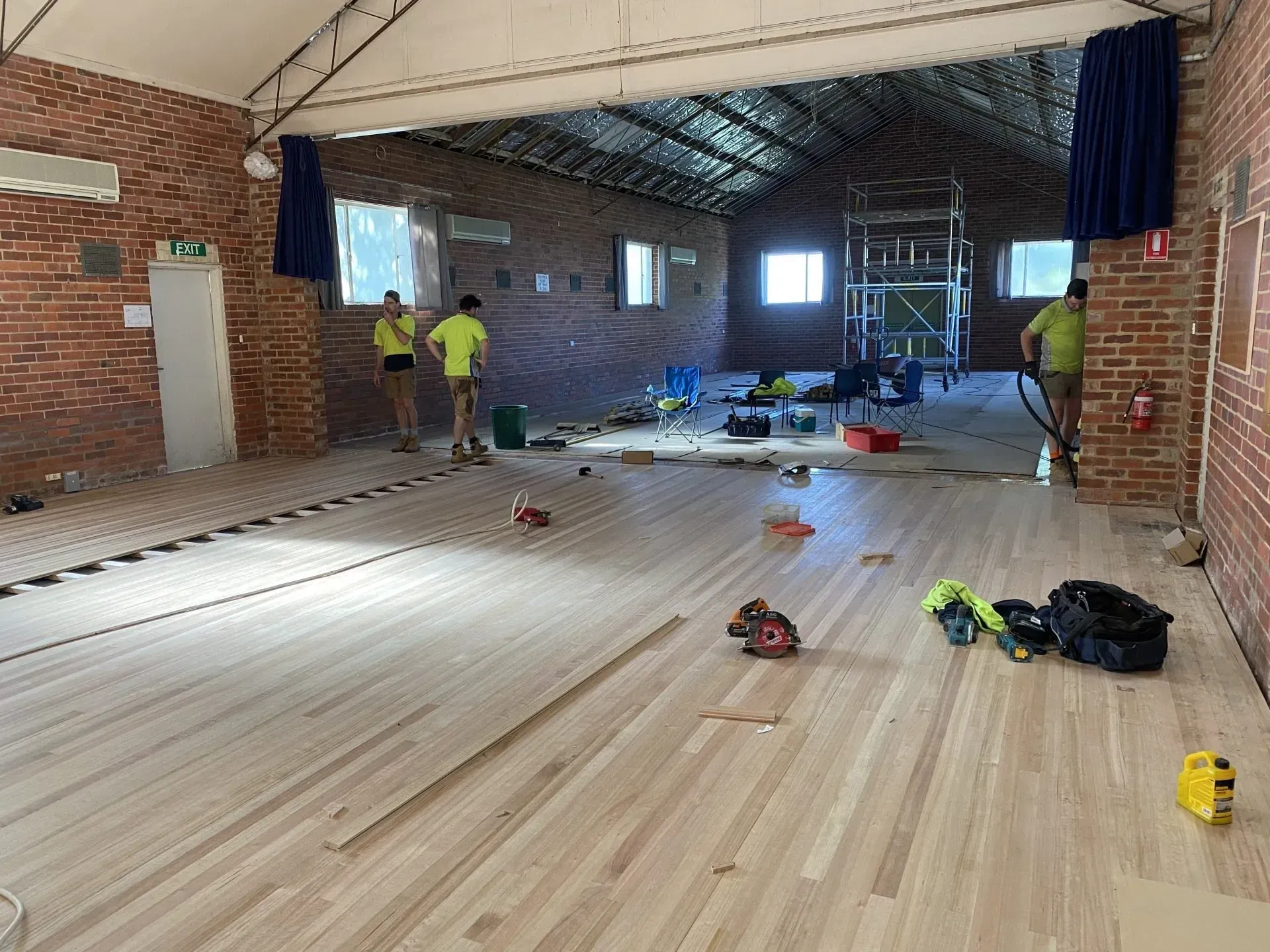 Workers inspect a damaged gym floor with debris scattered across the room.