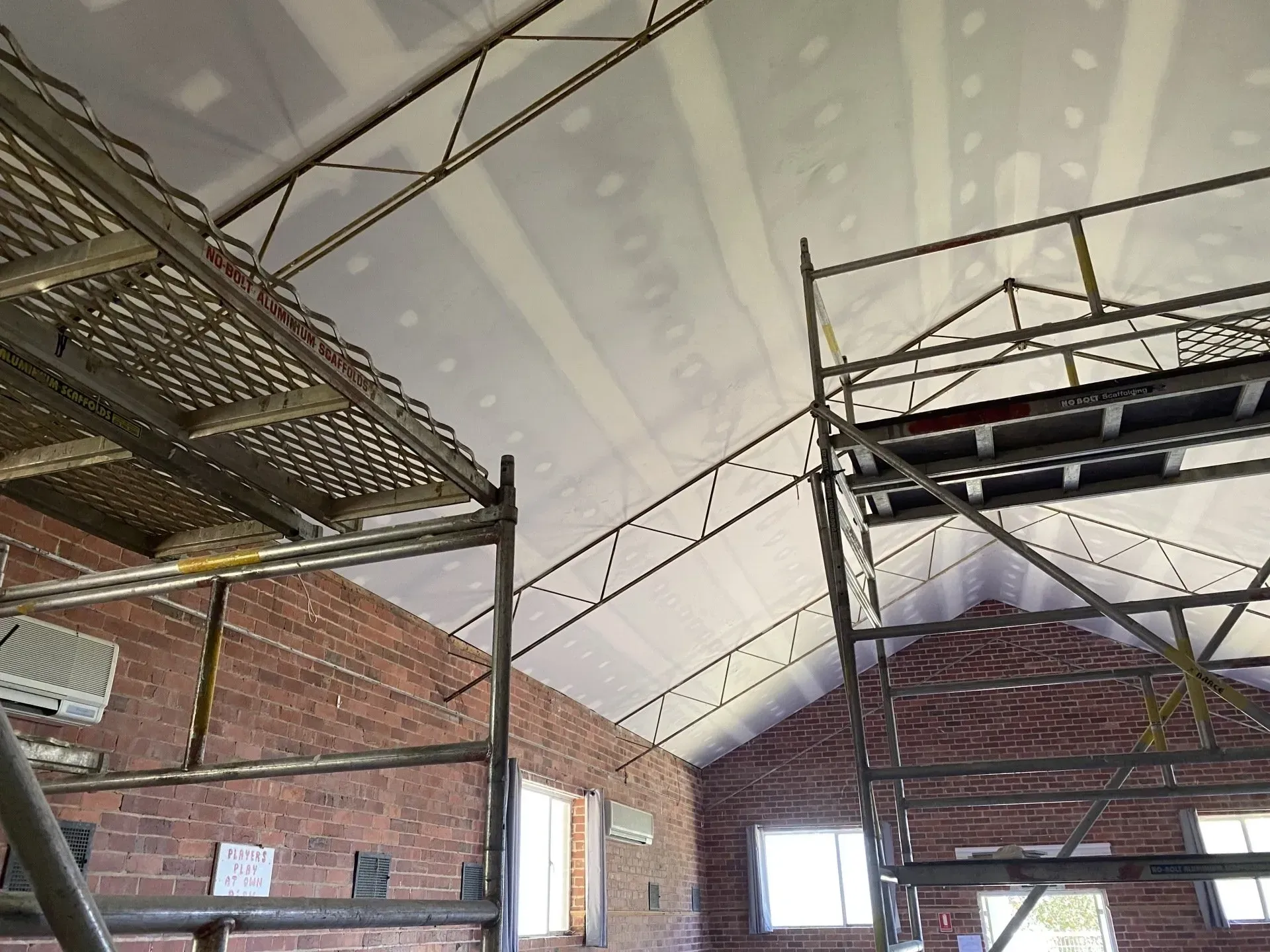 Scaffolding inside a brick building with a curved white ceiling under construction.