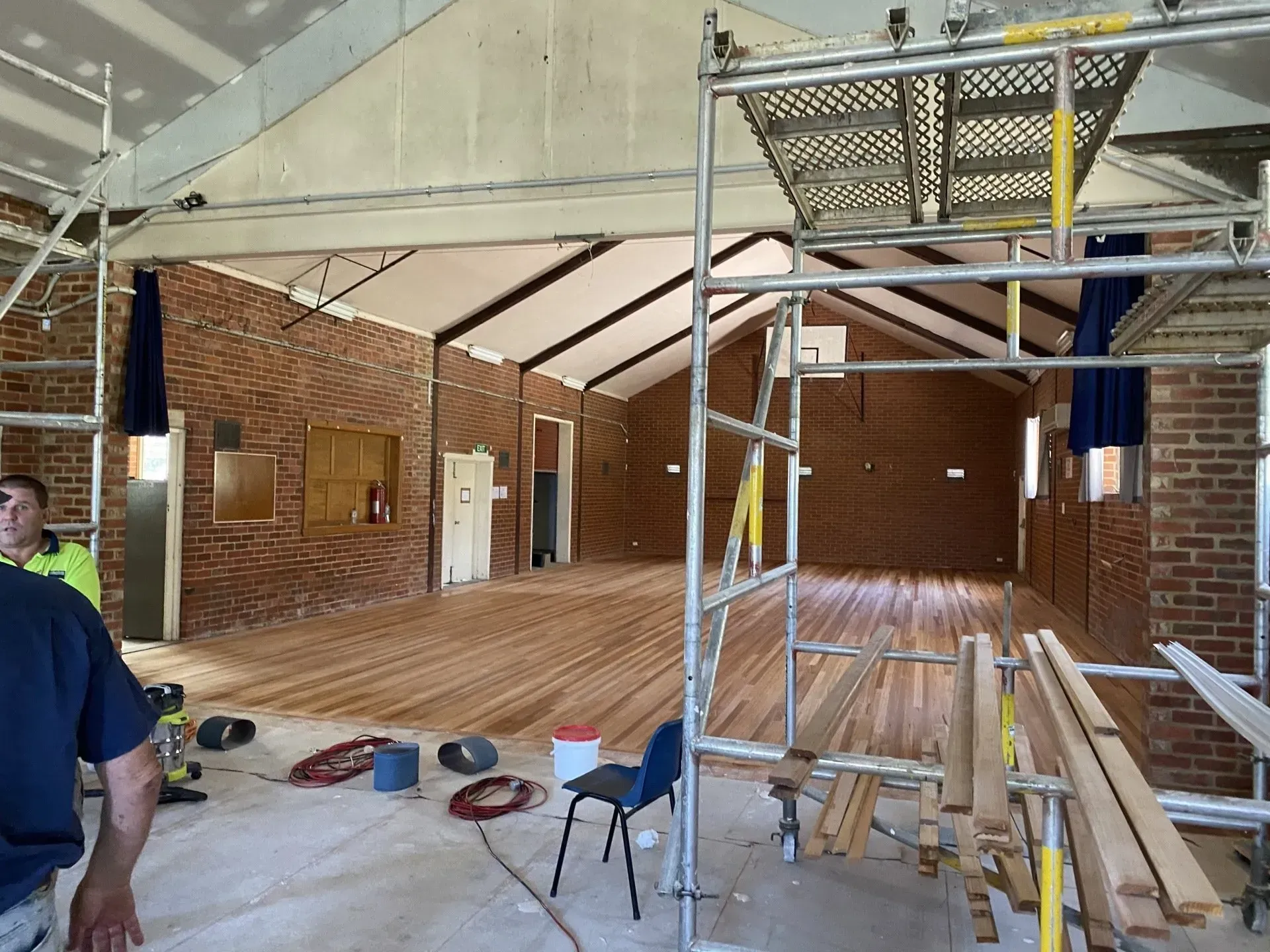 Interior of a brick building under renovation, with exposed beams, scaffolding, and construction tools on the floor.