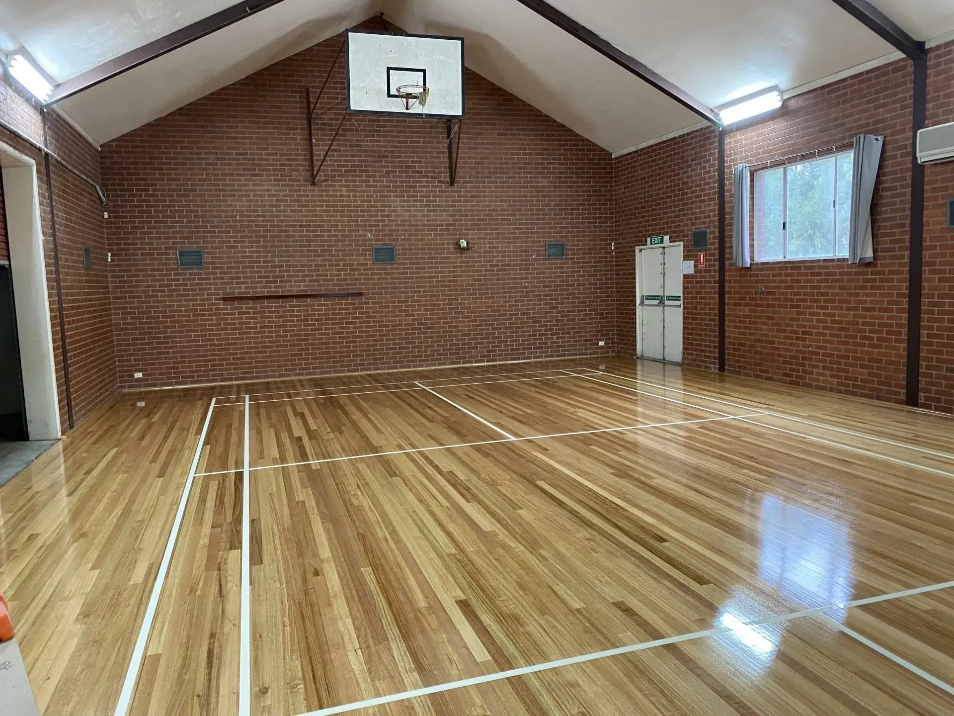 Empty indoor basketball court with polished wooden floor and brick walls