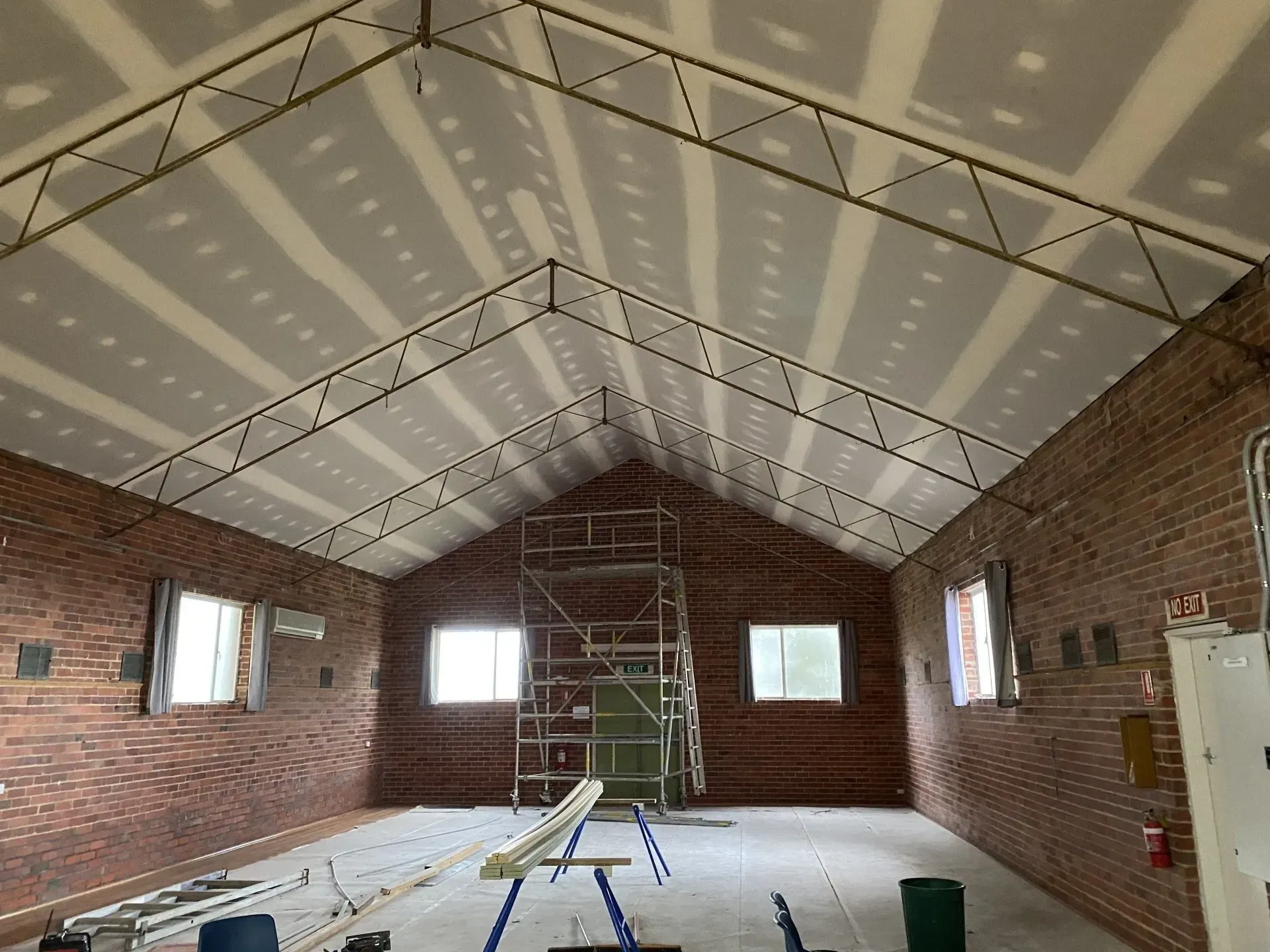 Brick-walled room under construction with scaffolding, exposed beams, and windows along both sides