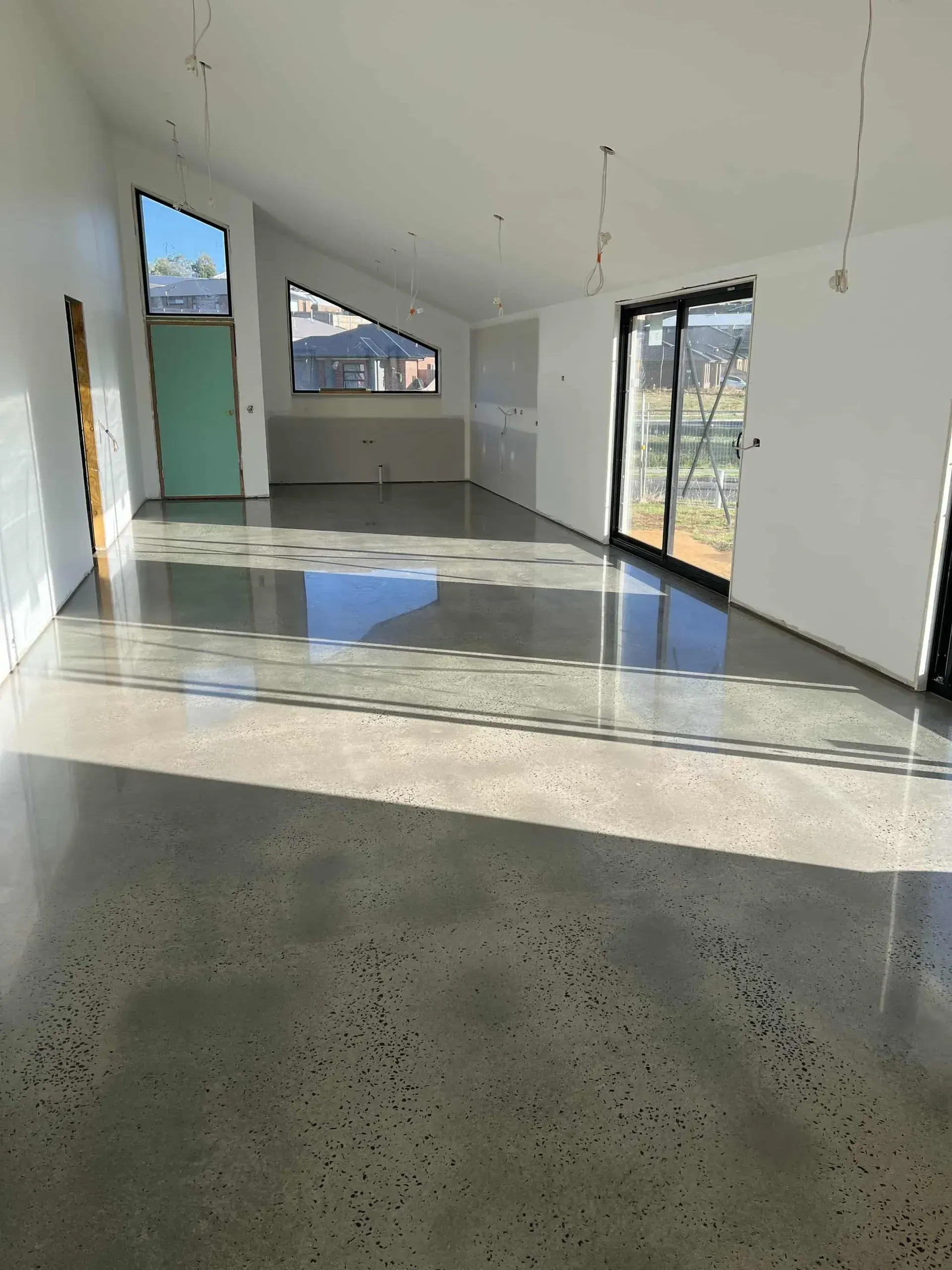 Empty sunlit room with concrete floor, white walls, and large windows and glass doors.