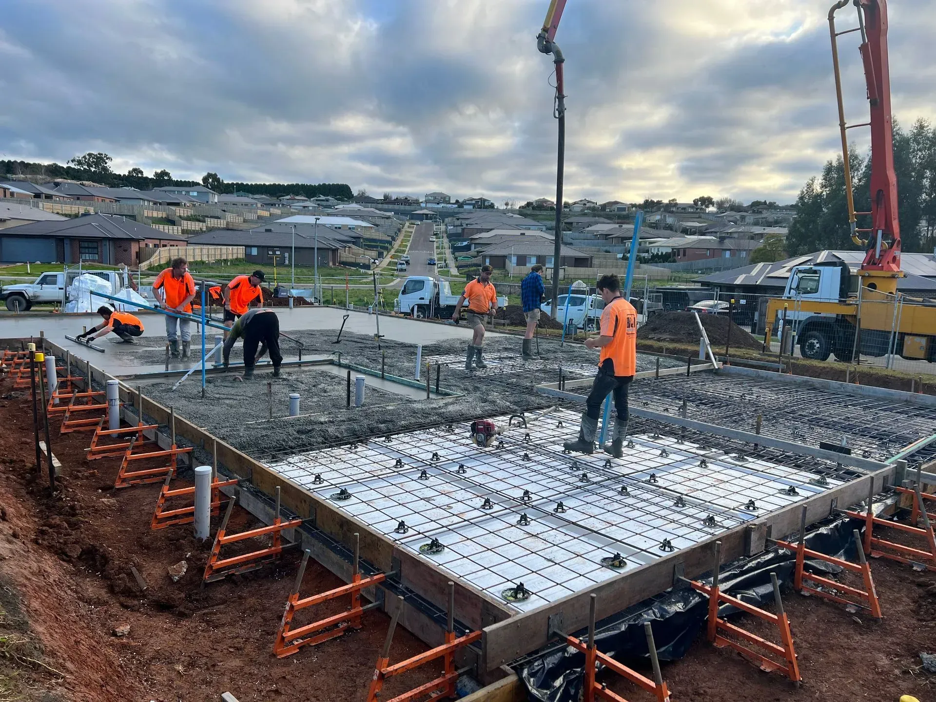 Construction crew pouring concrete foundation at a building site with orange-clad workers and machinery.