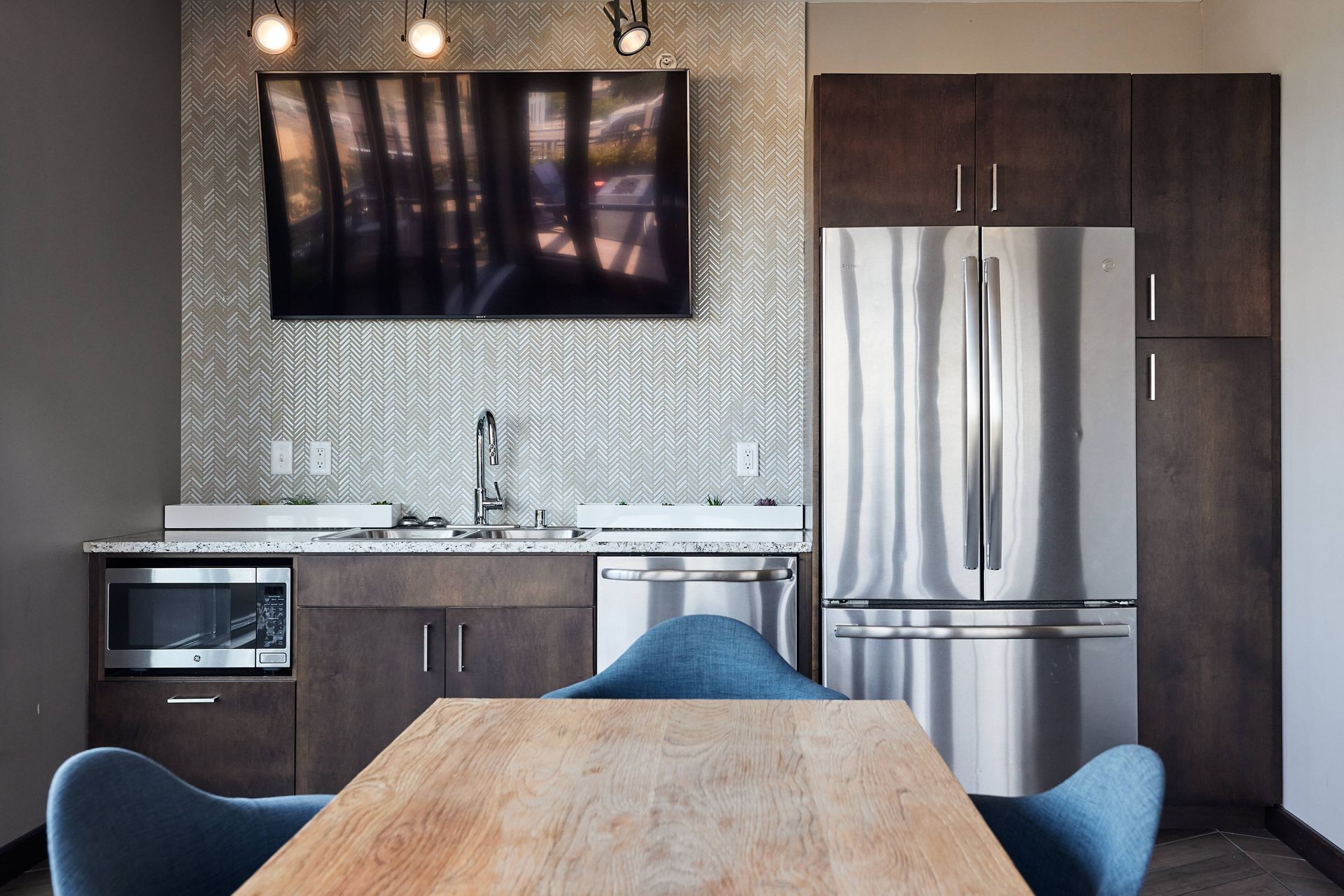 Kitchen with microwave, sink, and stainless steel refrigerator, plus a TV and wooden table.