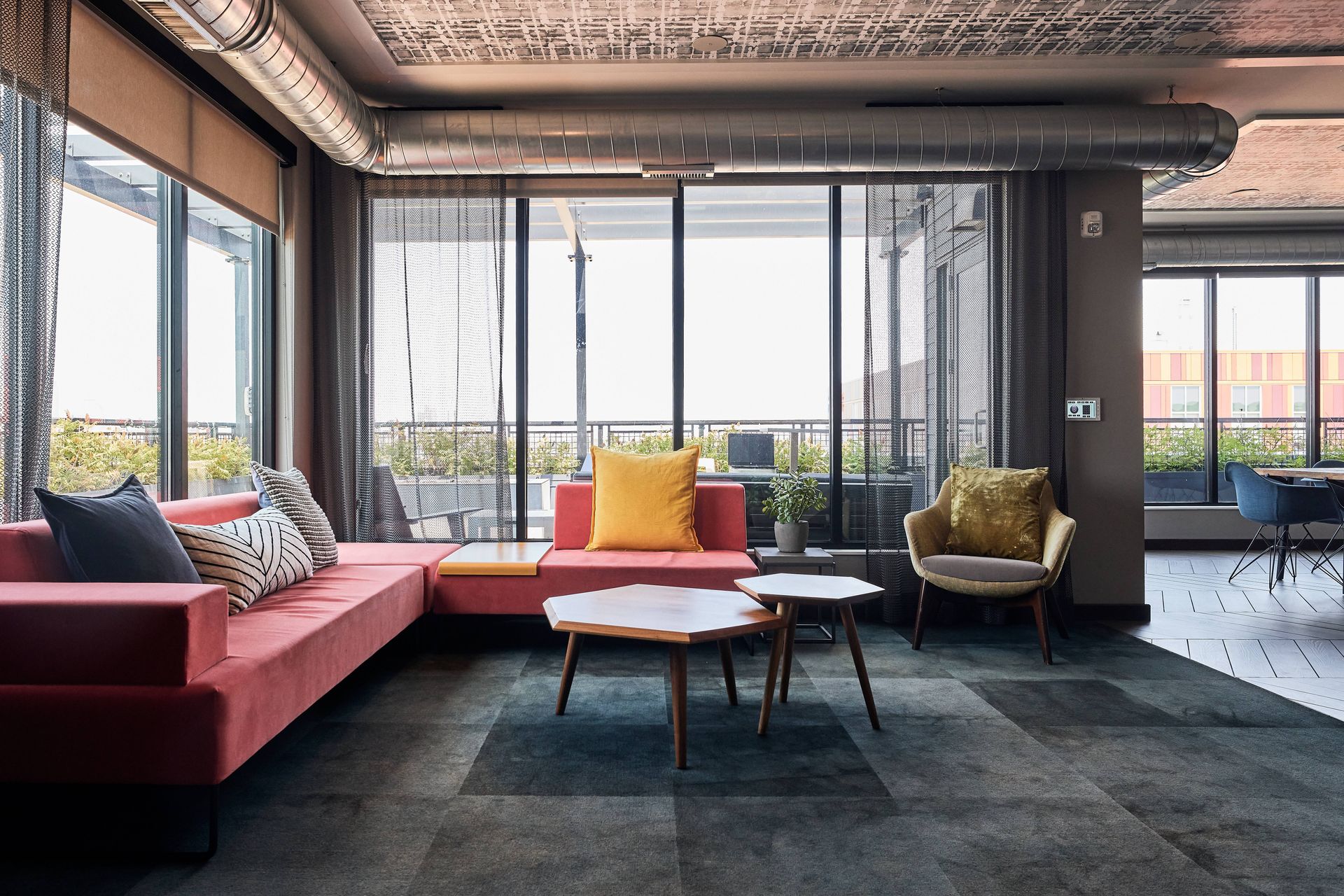A modern office lounge with a red sofa, armchairs, and coffee tables near large windows.