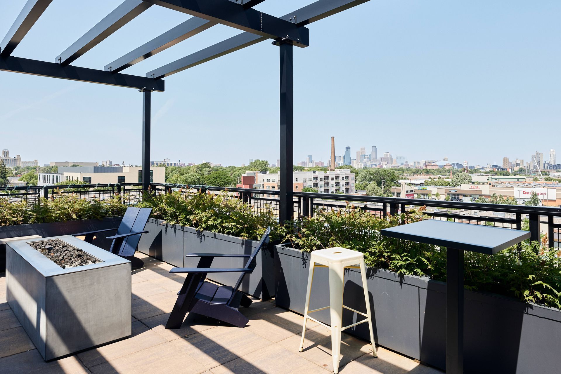 Rooftop patio with fire pit, seating, and city skyline view under a sunny sky.