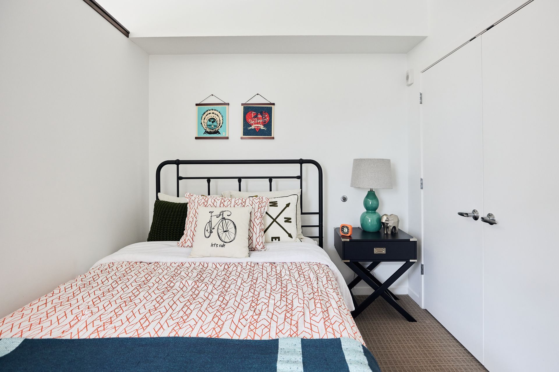 Bedroom with a metal bed frame, colorful bedding, a nightstand, and wall art.