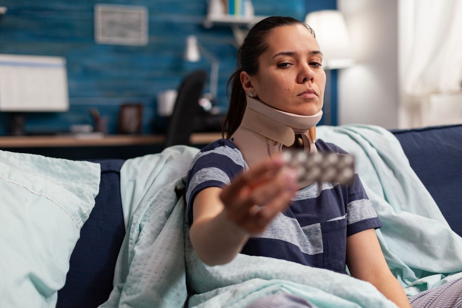 Woman in a neck brace sitting on a couch, reaching out with a card in a living room.