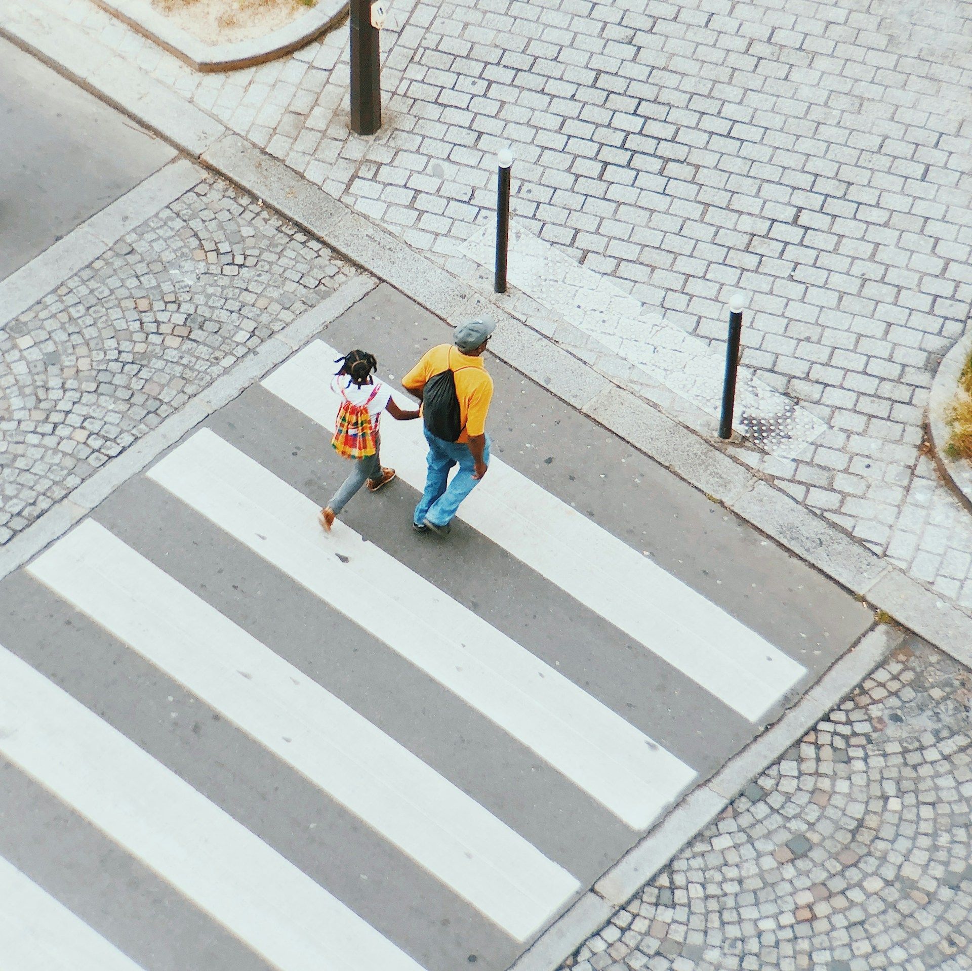 Two people crossing a street on a zebra crossing beside cobblestone pavement