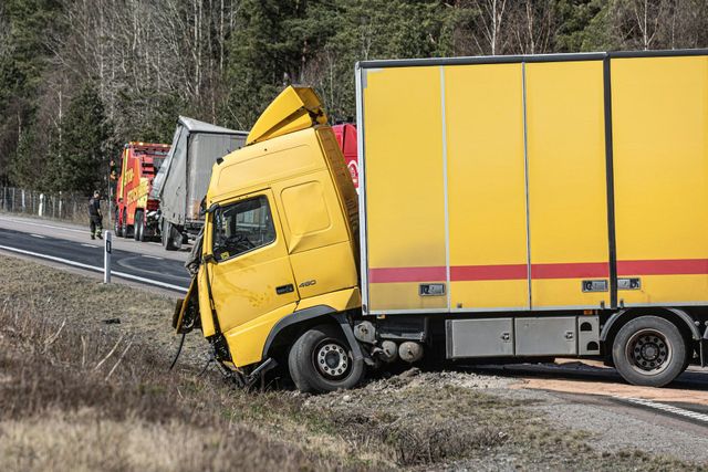 Yellow truck stuck in a roadside ditch beside a guardrail, with emergency vehicles nearby