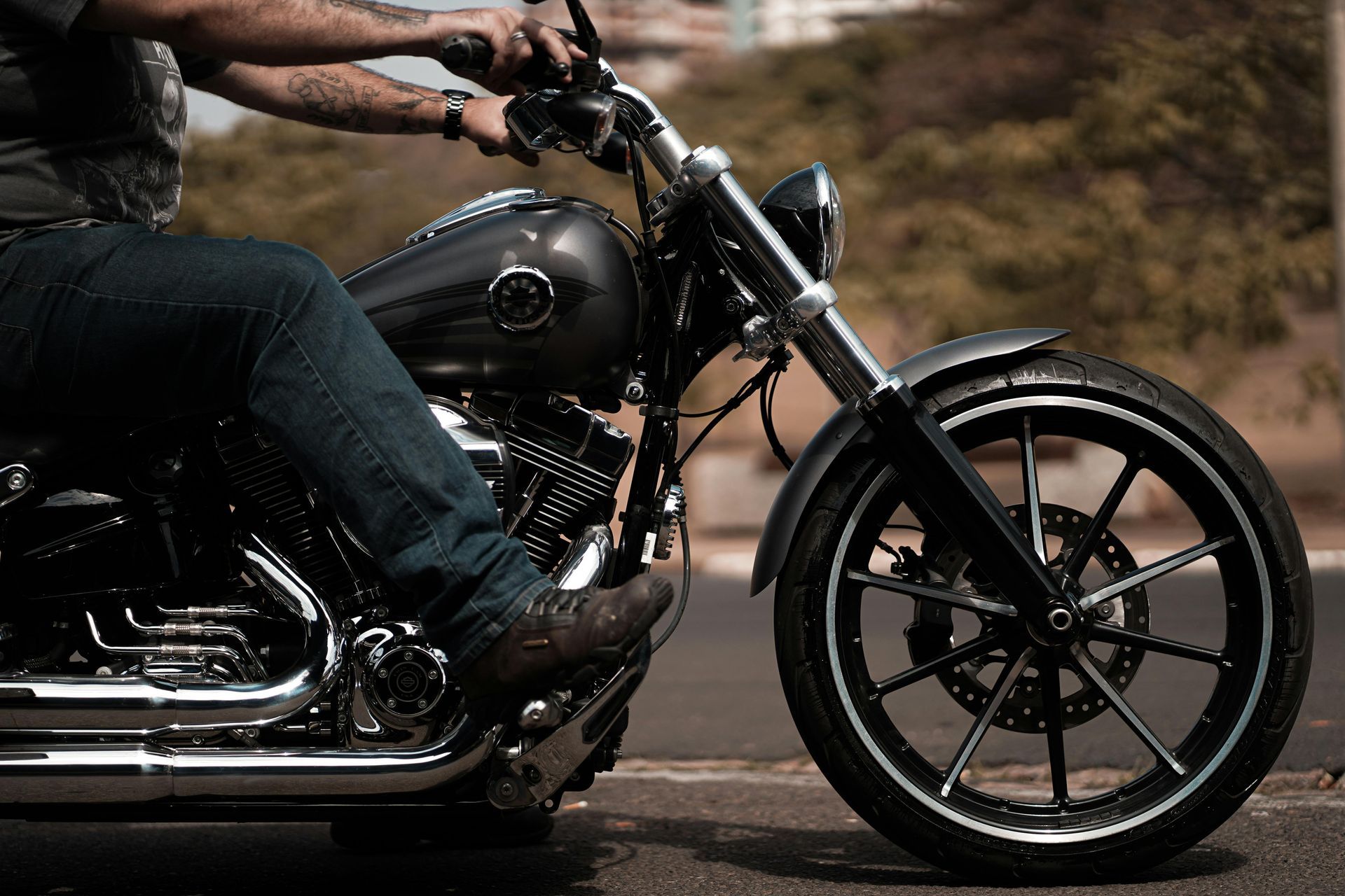 Rider on a black motorcycle cruising on a road, with a close-up view of the front wheel and engine.