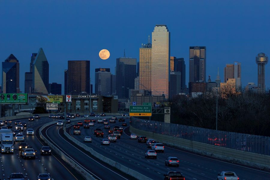 City skyline at dusk with a full moon above a busy highway and traffic in the foreground