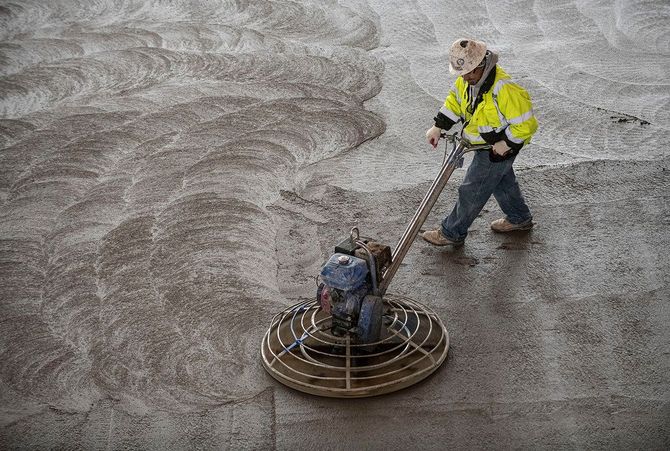 Construction worker using a power trowel to smooth wet concrete.