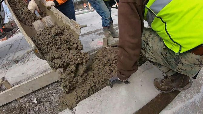 Construction crew pouring wet concrete from a chute into a form.