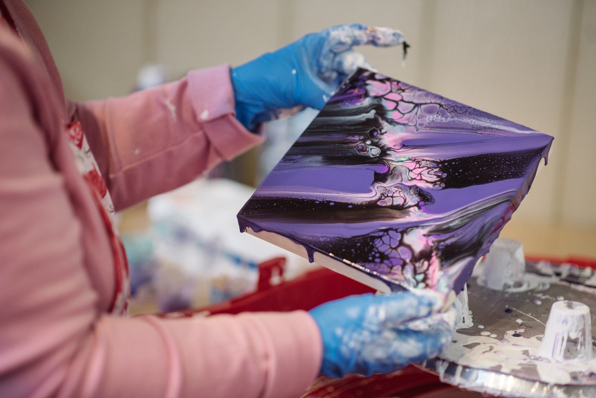 Gloved hands holding a black-and-purple marbled art piece over a worktable