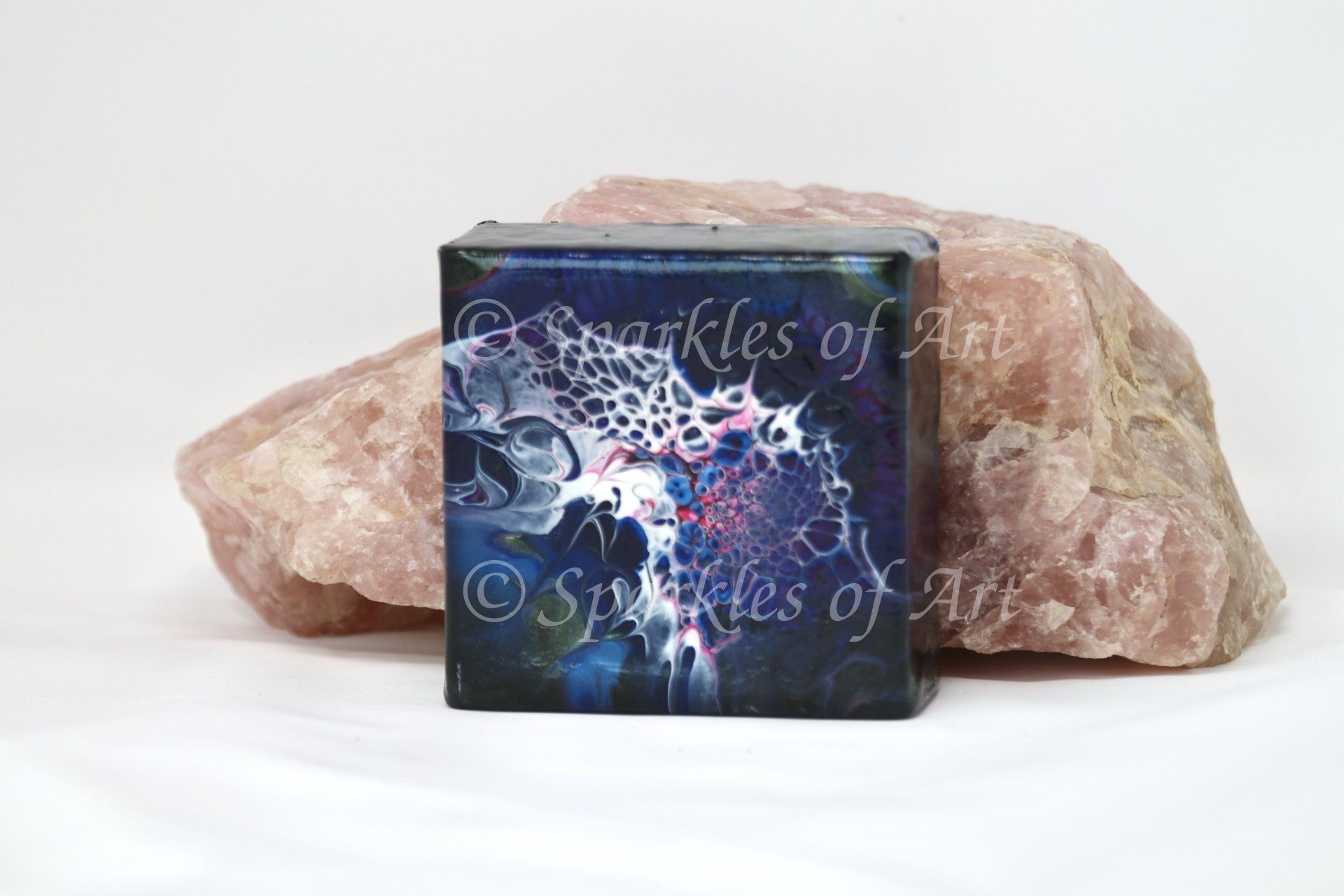 Square artwork in front of two pink crystals on a white background