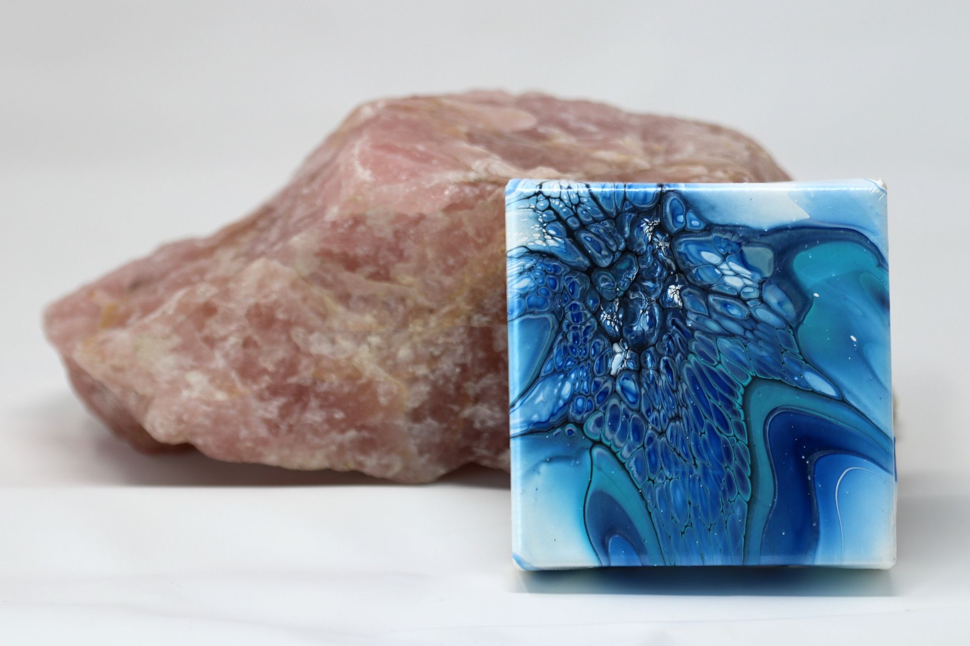 Blue glass cube with abstract crackle pattern in front of a pink stone on a white surface
