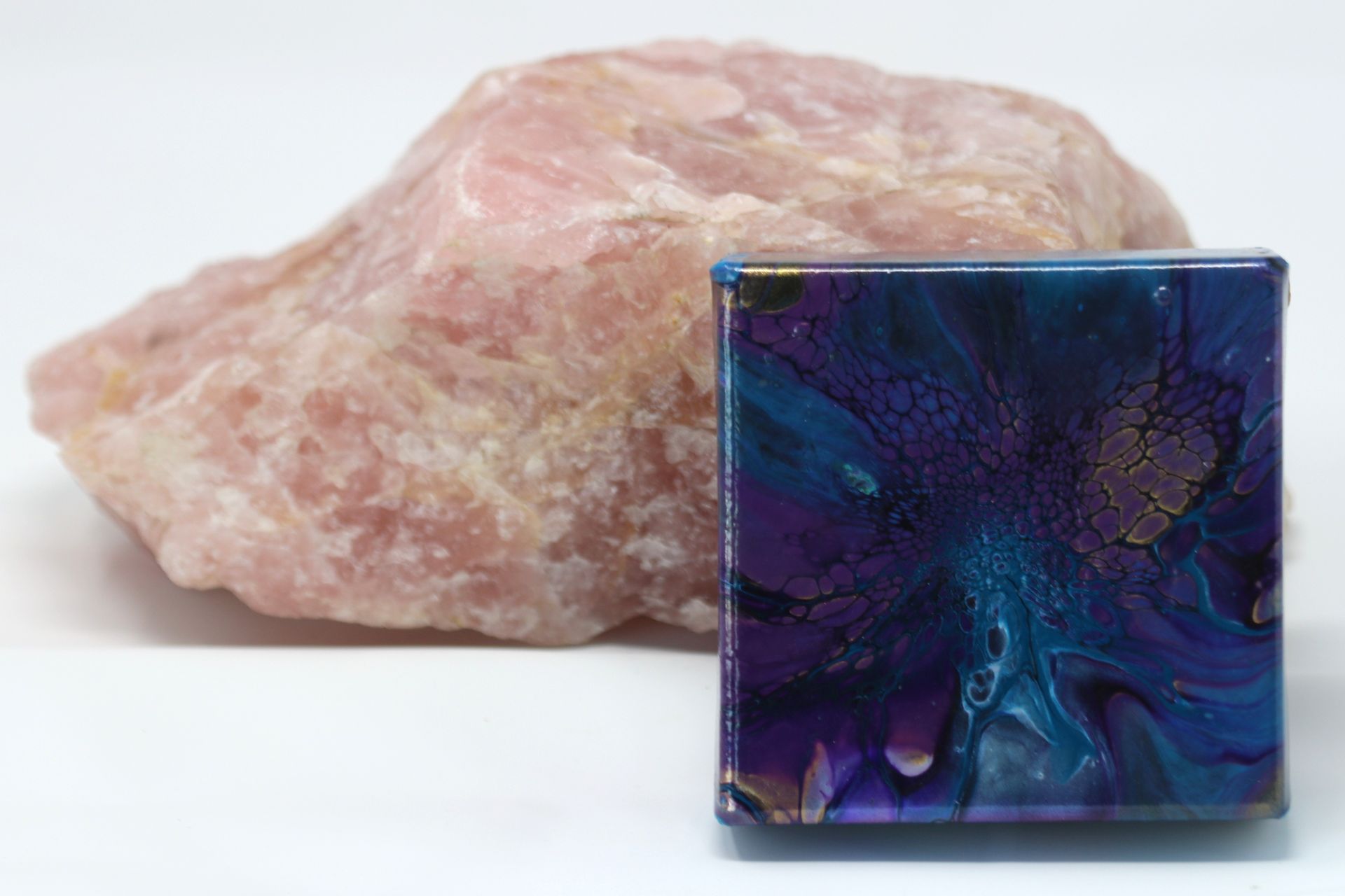 Pink crystal behind a small iridescent blue-purple glass cube on a white surface