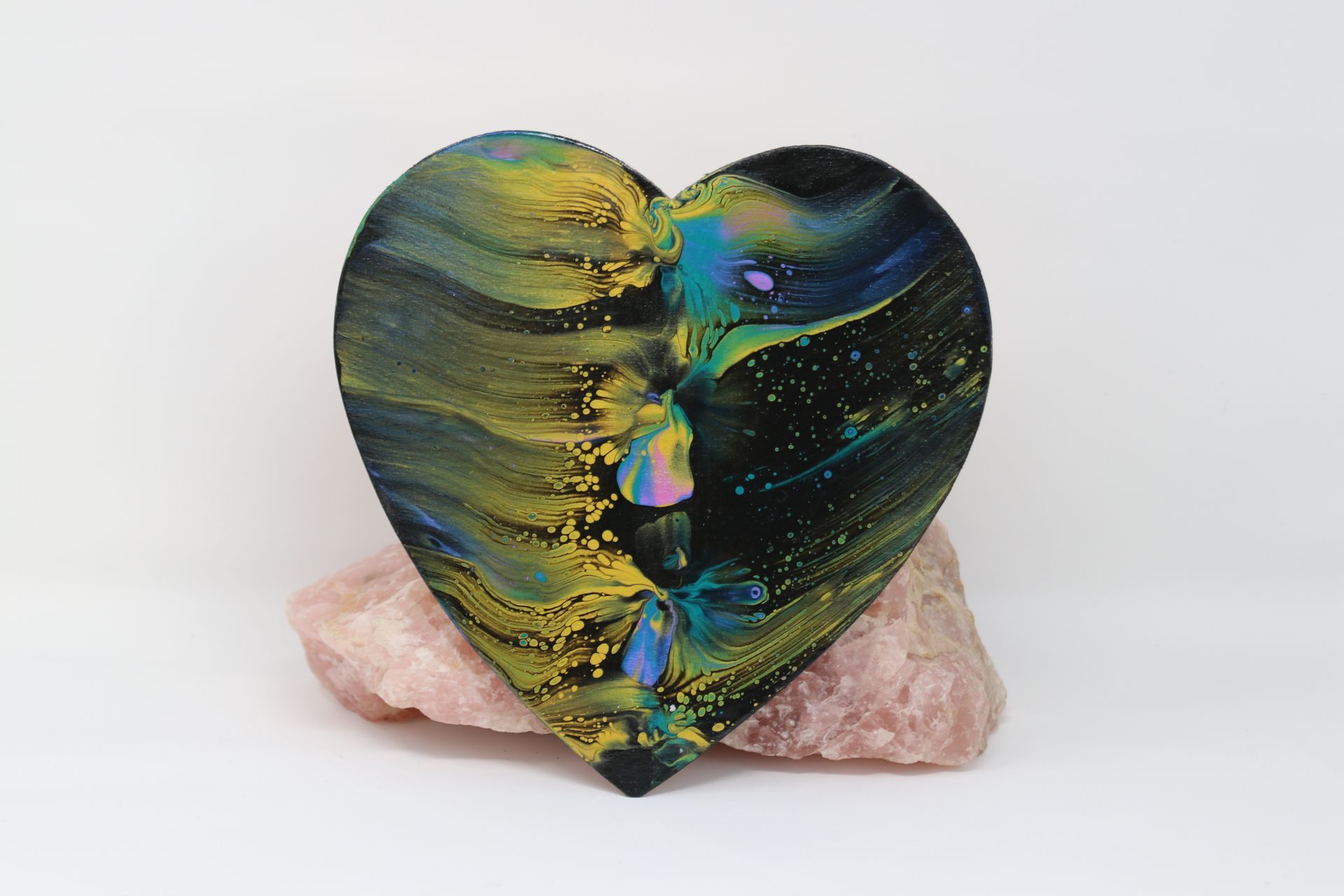 Iridescent heart-shaped stone in blue, green, and gold on a pale pink crystal base