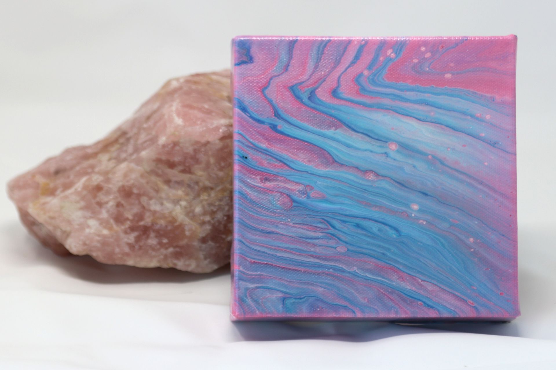 Pink and blue swirled square stone beside a rough tan rock on a white background