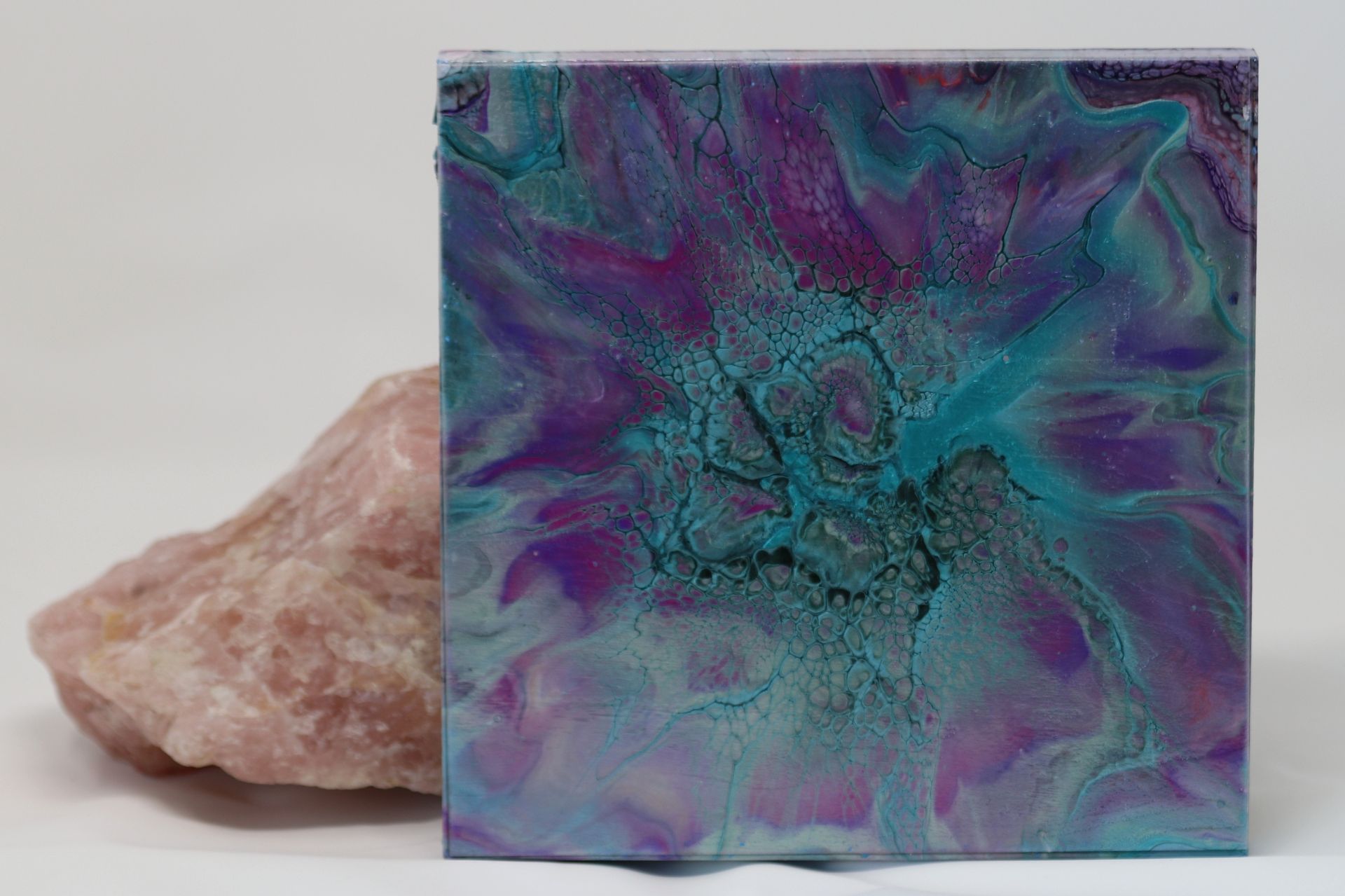 Abstract teal and purple square artwork beside a pink rock on a light background