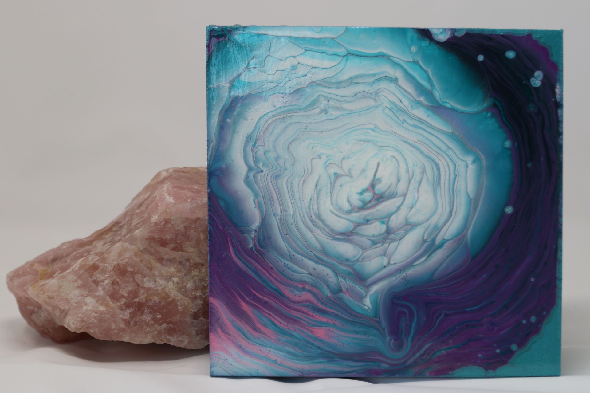 Rose quartz beside a blue, purple, and white abstract agate-style painting