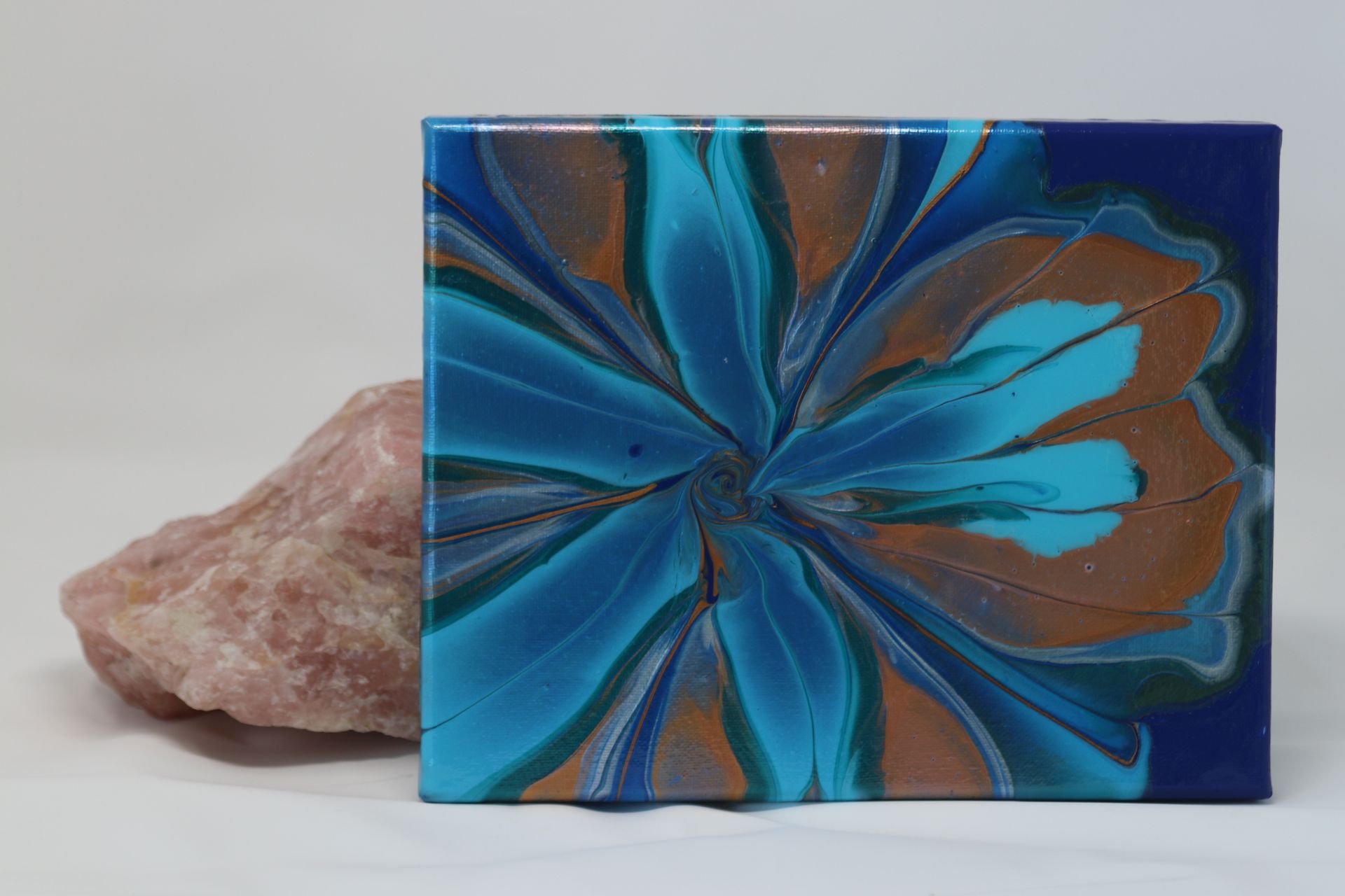 Blue and orange abstract flower design on a square tile beside a pink crystal rock