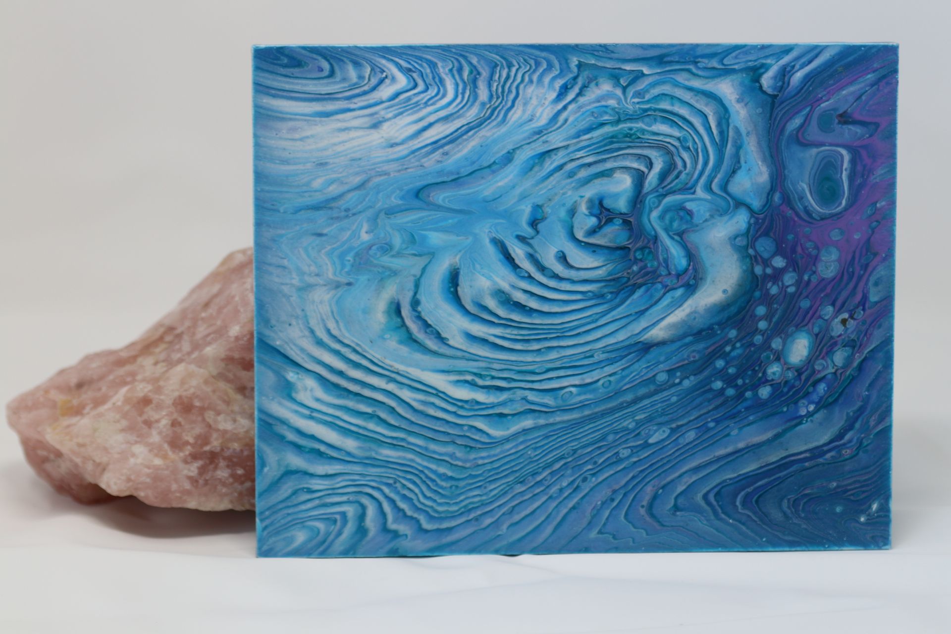 Blue marbled art panel beside a pink rock on a light background