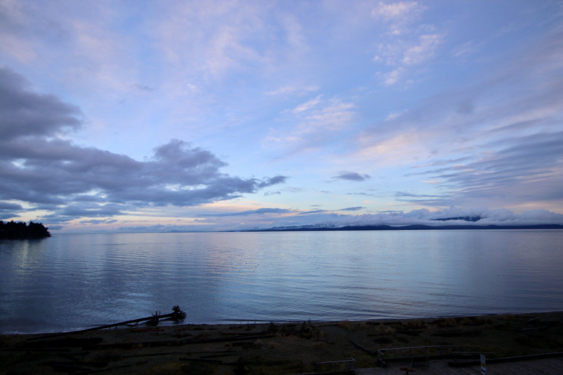 Calm ocean at dusk with blue clouds and a dark shoreline in the foreground