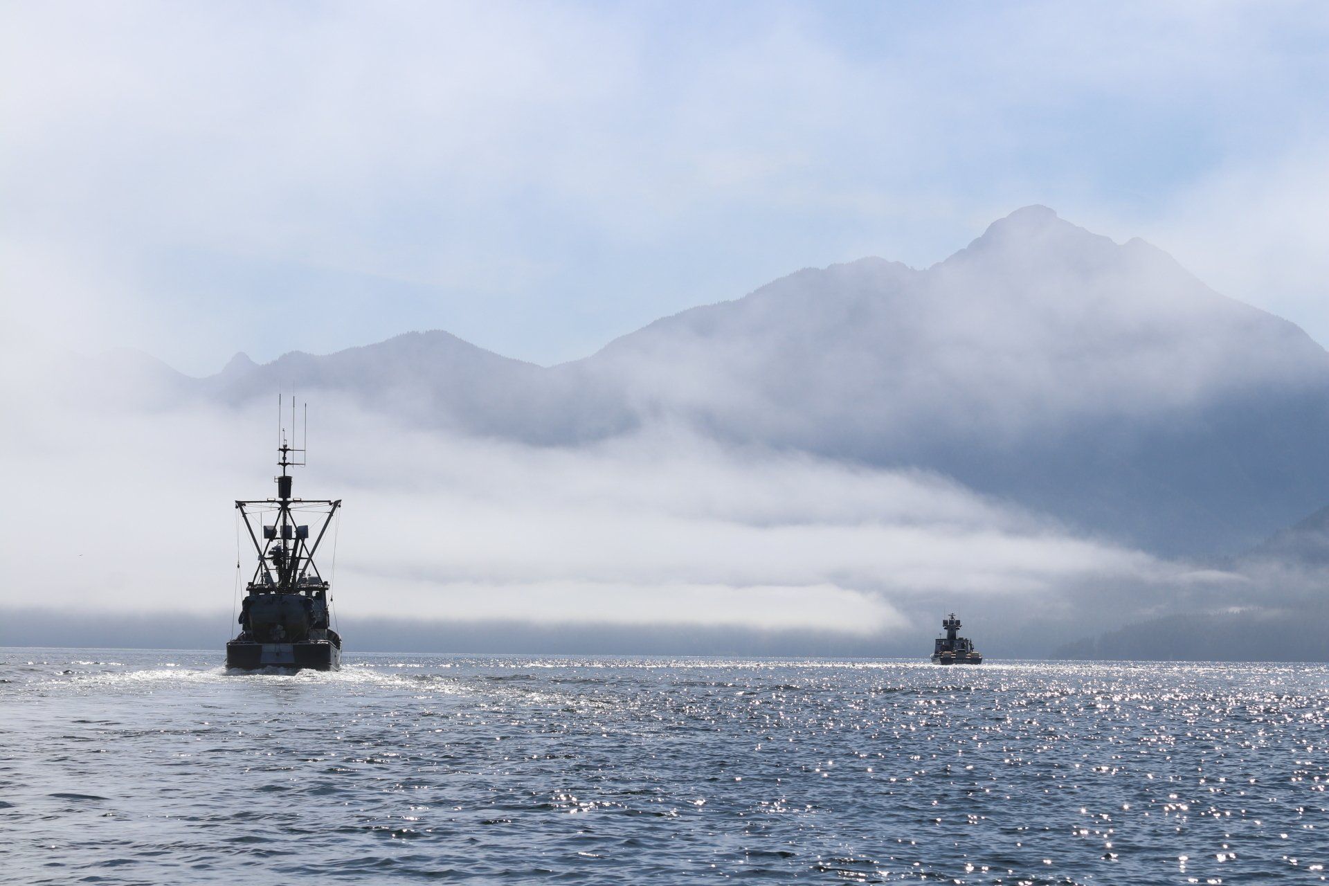 Naval ship and small boat on sparkling sea with misty mountains in the background