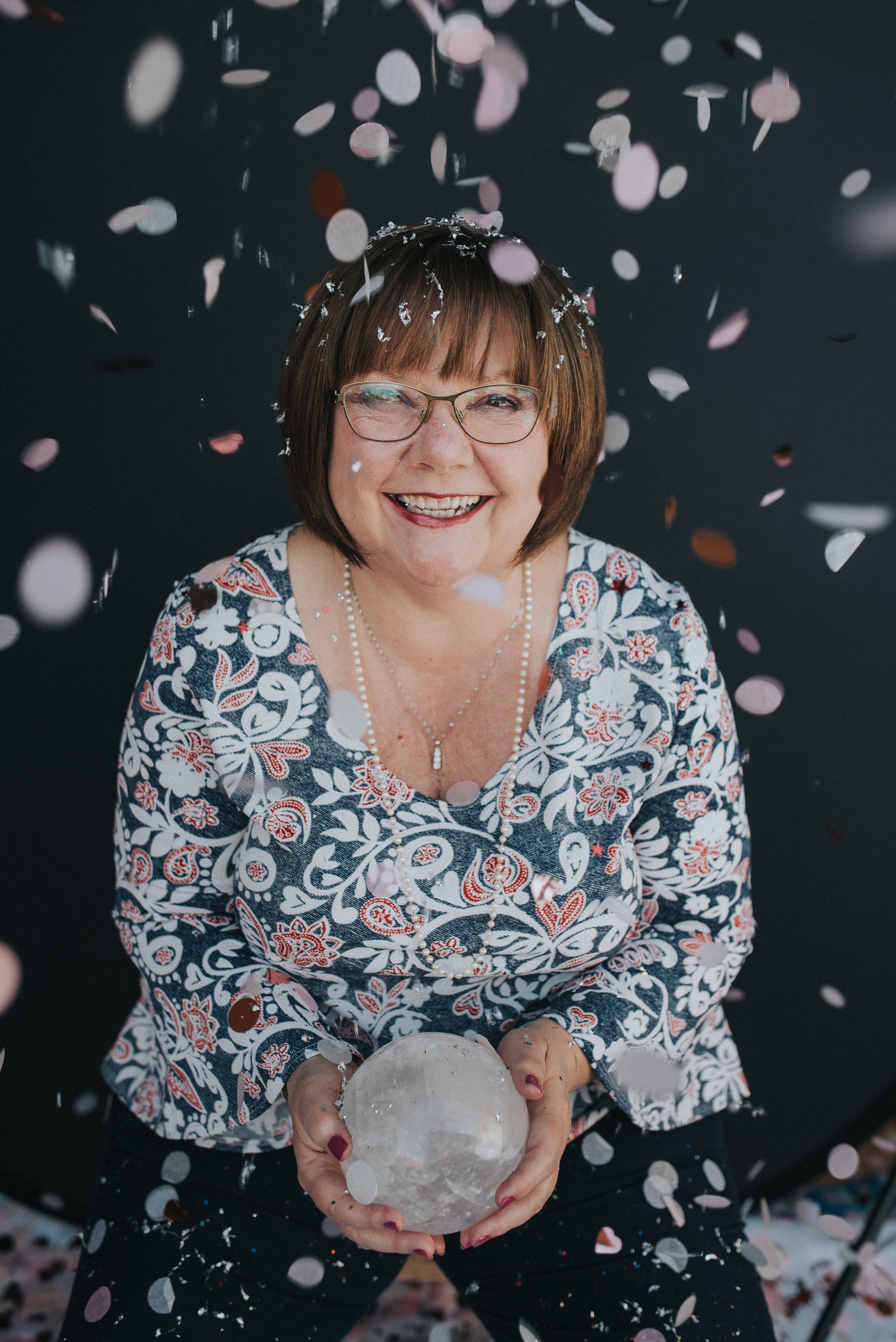 Smiling person holds a clear crystal ball as pink petals fall against a dark background