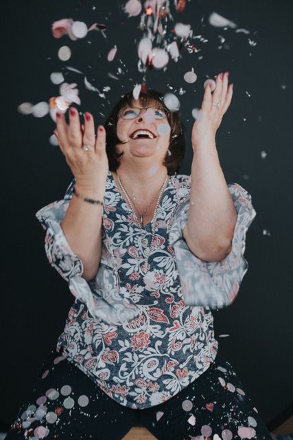 Woman in floral top throwing white confetti upward against a dark background