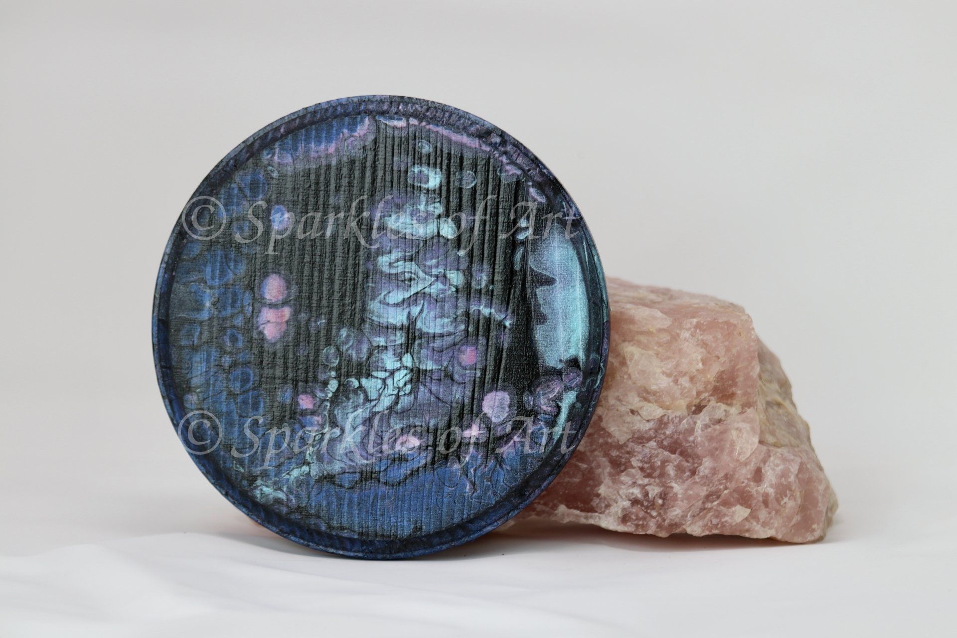 Blue iridescent round object leaning against a pink crystal on a white background