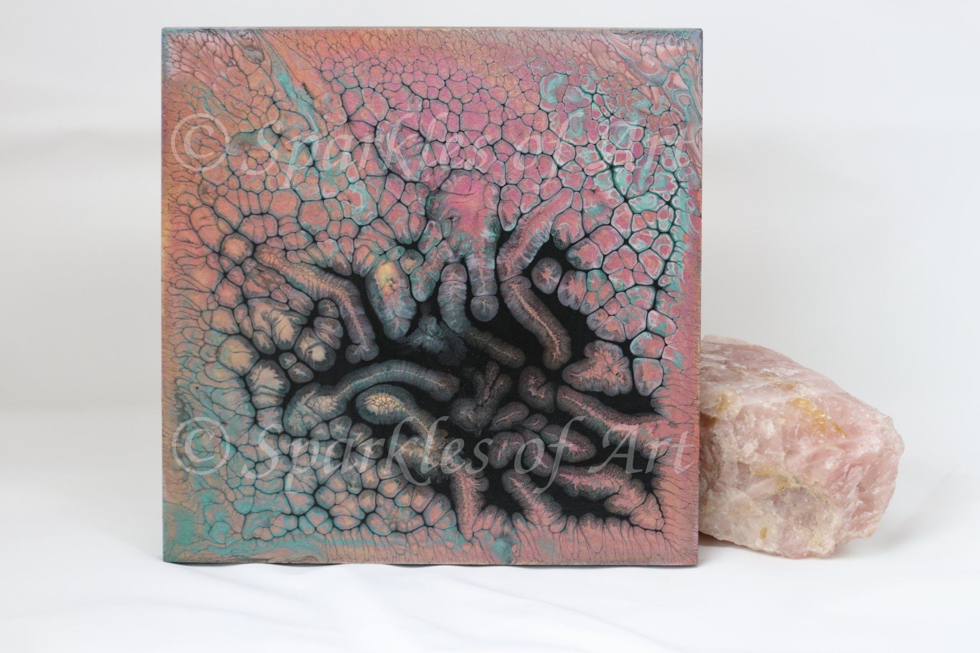 Abstract square artwork with teal and pink cracks, black swirling center, beside a pale crystal.