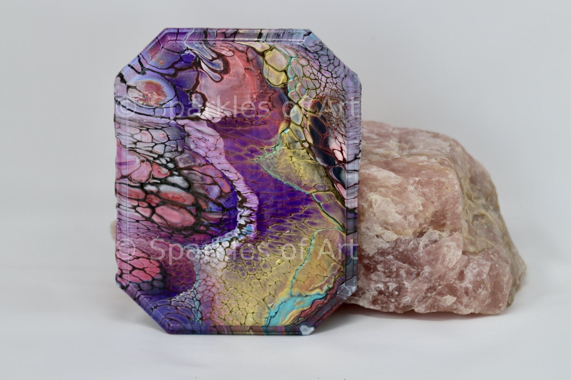 Colorful iridescent geode-like slab beside a pale pink crystal on a white background